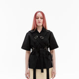 Front view of the Emily Millichip Bondage Shirt in black cotton canvas, showing cross straps, stainless steel buckles, oversized patch pockets and a waist belt.