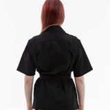 Back view of the Emily Millichip Bondage Shirt in black cotton canvas, showing short sleeves, a structured collar, and a canvas belt cinching the waist.