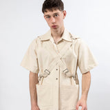 Front view of the Emily Millichip Bondage Shirt in natural seeded cotton canvas, worn loose with crossed straps, stainless steel buckles and oversized patch pockets