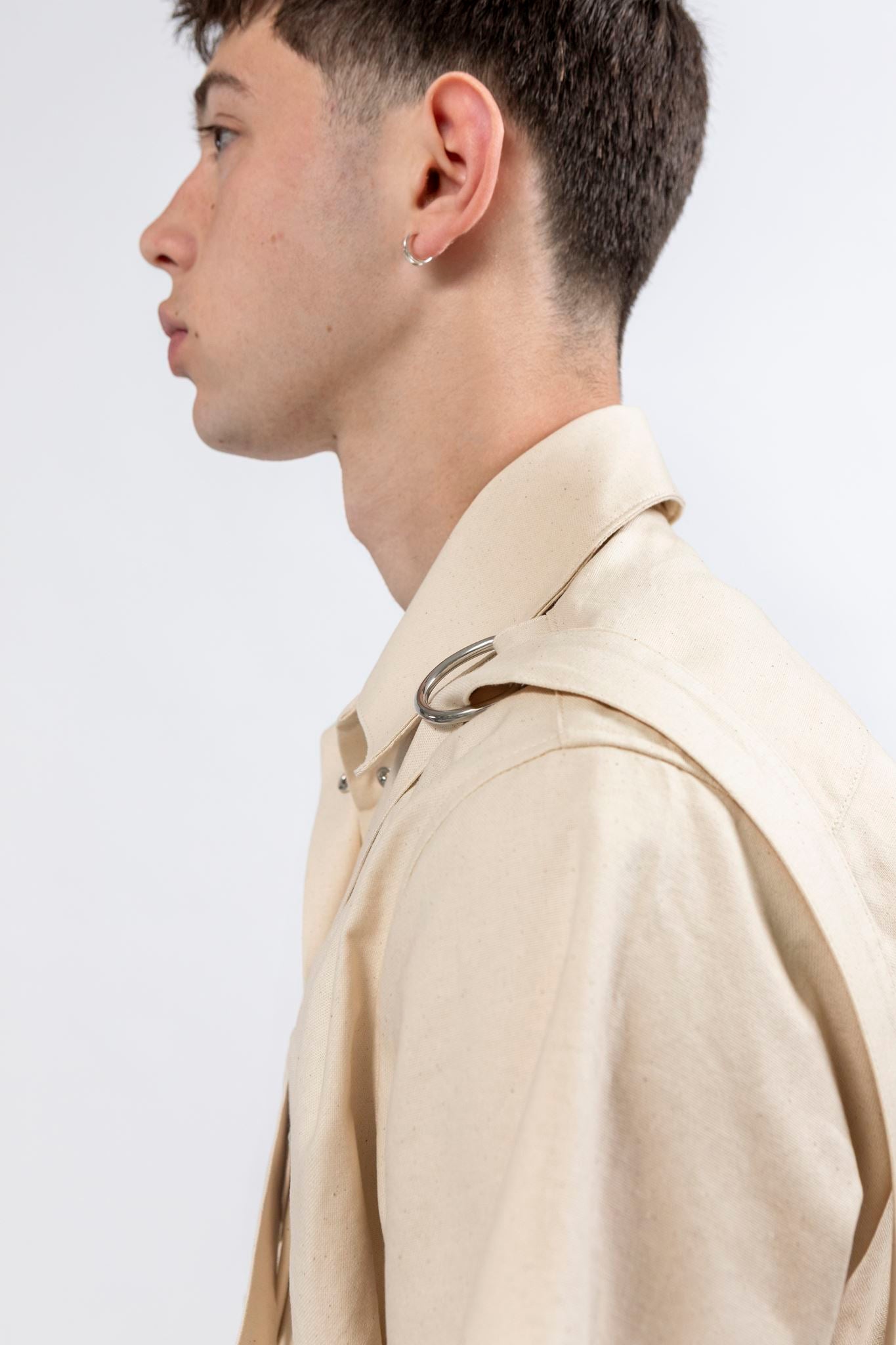 Side profile of the Emily Millichip Bondage Shirt in natural seeded cotton canvas, showing the camp collar, shouder strap, and stainless steel d-ring detail.