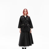 Full-length front view of the Emily Millichip Gravity Field Jacket in black heavyweight sanded canvas, worn with  relaxed boxy fit, zipped utility pockets, styled with a matching long black skirt.