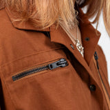 Close-up of the Emily Millichip Gravity Field Jacket in bronze heavyweight sanded canvas, showing the horizontal chest zip pocket, collar, black metal press studs and fabric texture.