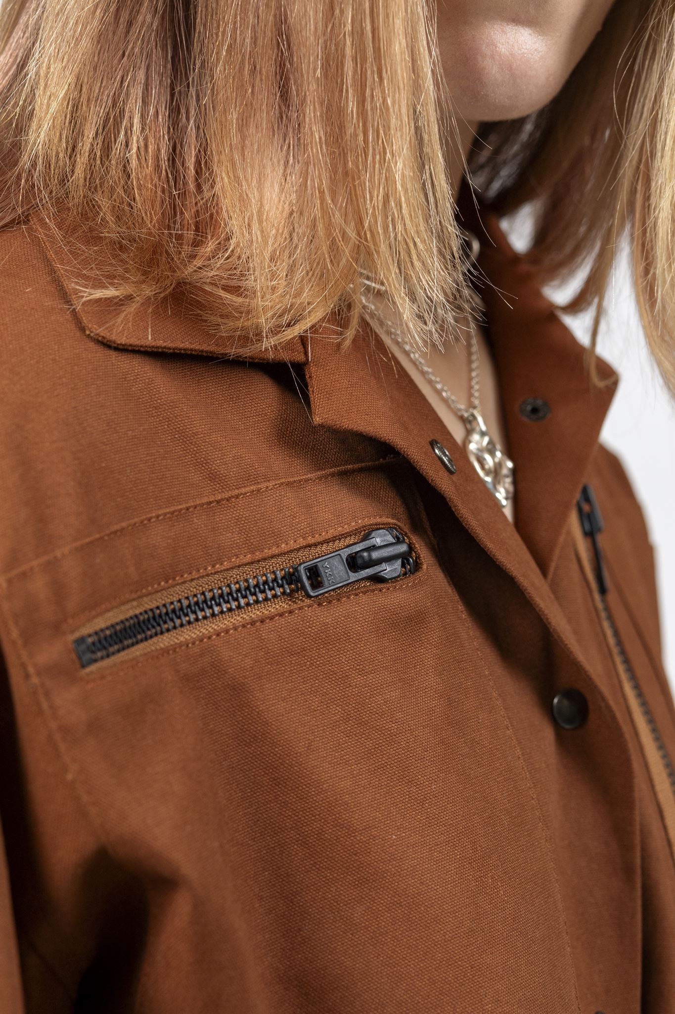 Close-up of the Emily Millichip Gravity Field Jacket in bronze heavyweight sanded canvas, showing the horizontal chest zip pocket, collar, black metal press studs and fabric texture.