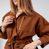 Three-quarter close-up of the Emily Millichip Gravity Field Jacket in bronze heavyweight sanded canvas, showing the zip chest pocket, cinched waist, fabric belt and oversized utility pockets