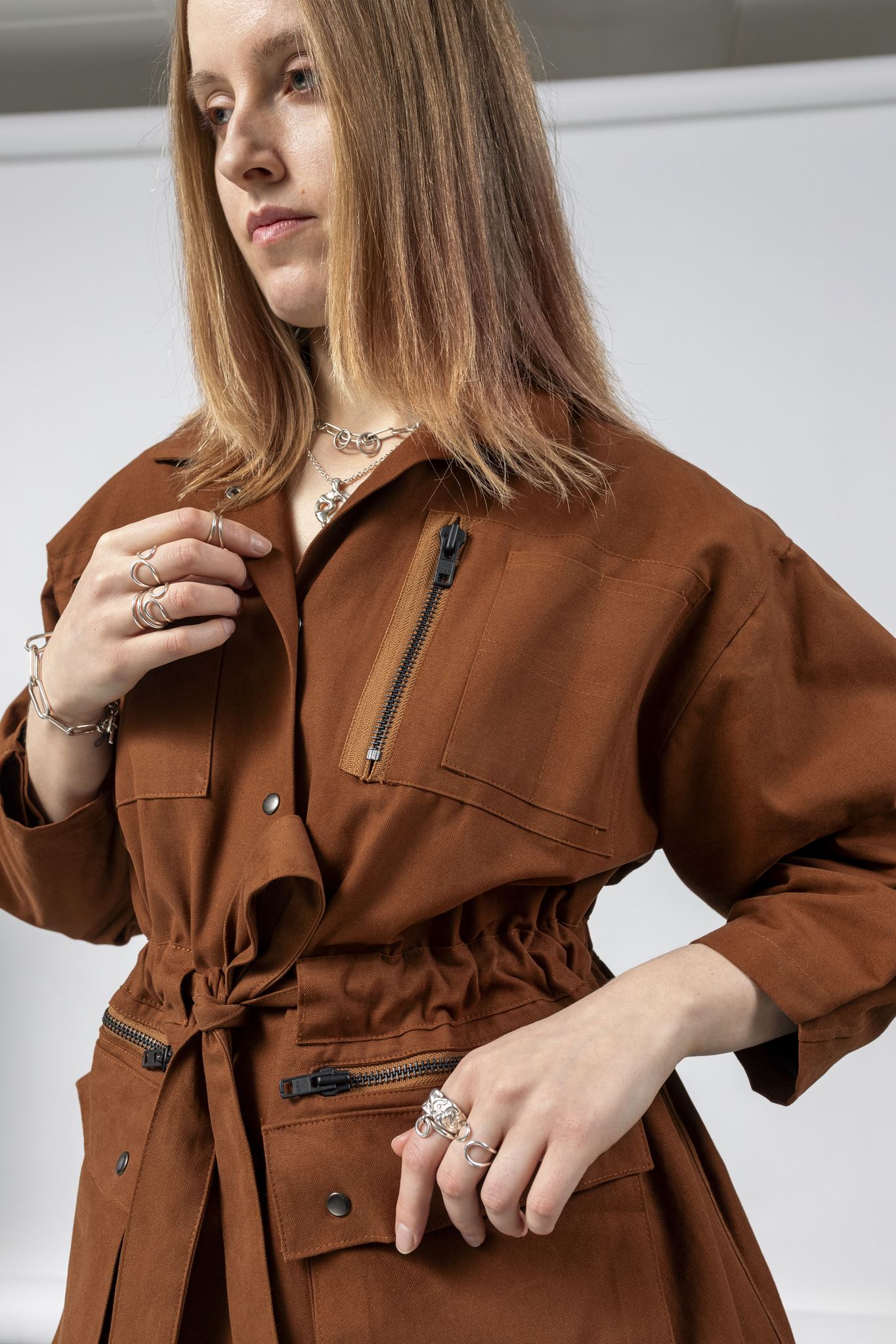Three-quarter close-up of the Emily Millichip Gravity Field Jacket in bronze heavyweight sanded canvas, showing the zip chest pocket, cinched waist, fabric belt and oversized utility pockets