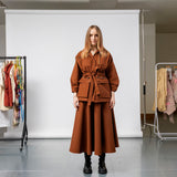Emily Millichip Gravity Field Jacket in bronze heavyweight sanded canvas, front view showing the adjustable drawstring waist, oversized utility pockets, and cropped sleeves, styled with a matching skirt.