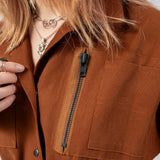 Close up of the Emily Millichip Gravity Field Jacket in bronze heavyweight sanded canvas, showing the vertical black oxidised metal zip, chest utility pocket, press stud fastening and fabric texture.